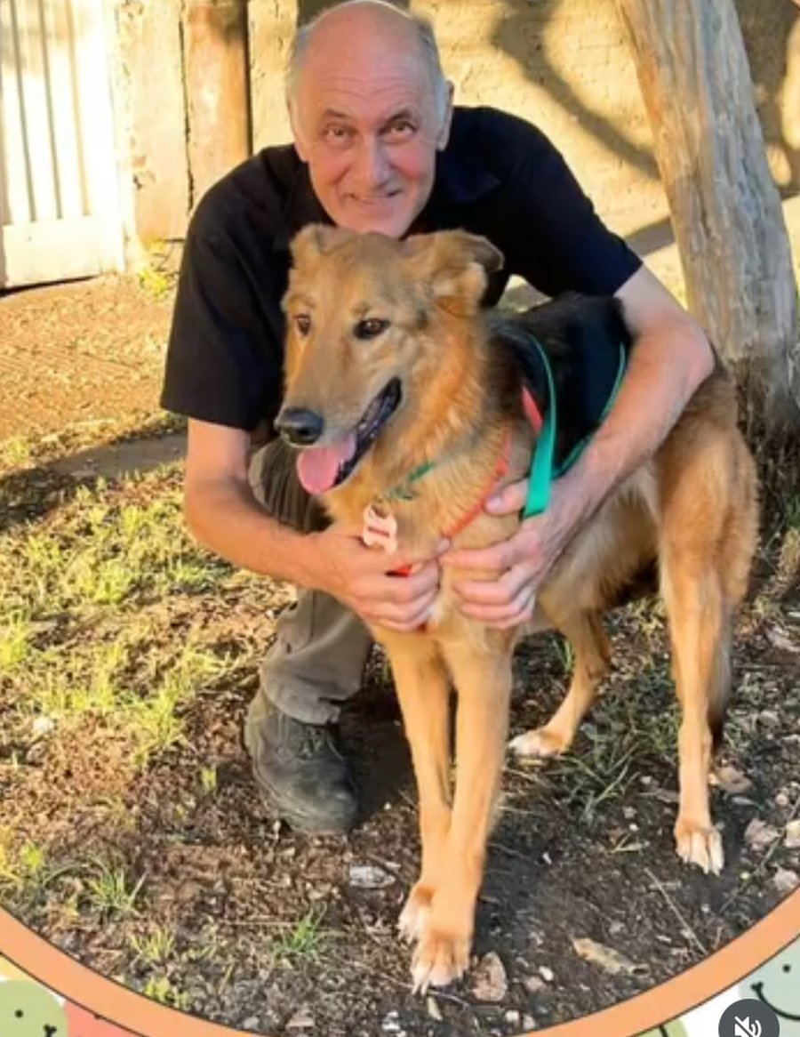 Un voluntario abrazando a un perro rescatado, sonriendo mientras posa con él al aire libre.